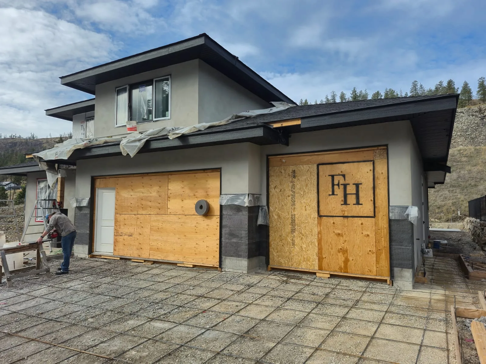 Front of the Lot 42 home with stucco walls, boarded garage openings and a crew member working on the driveway.