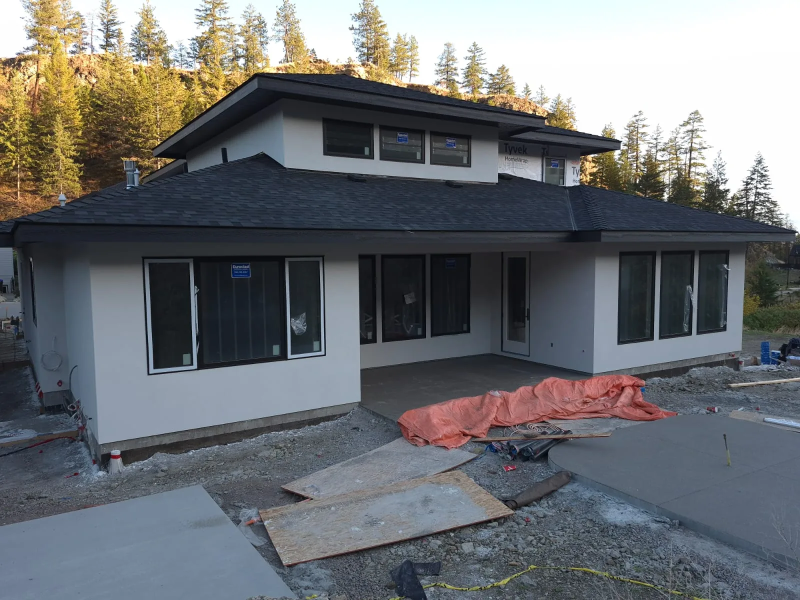 Rear elevation of the Lot 42 home with a finished light grey stucco exterior and covered patio, autumn trees behind.