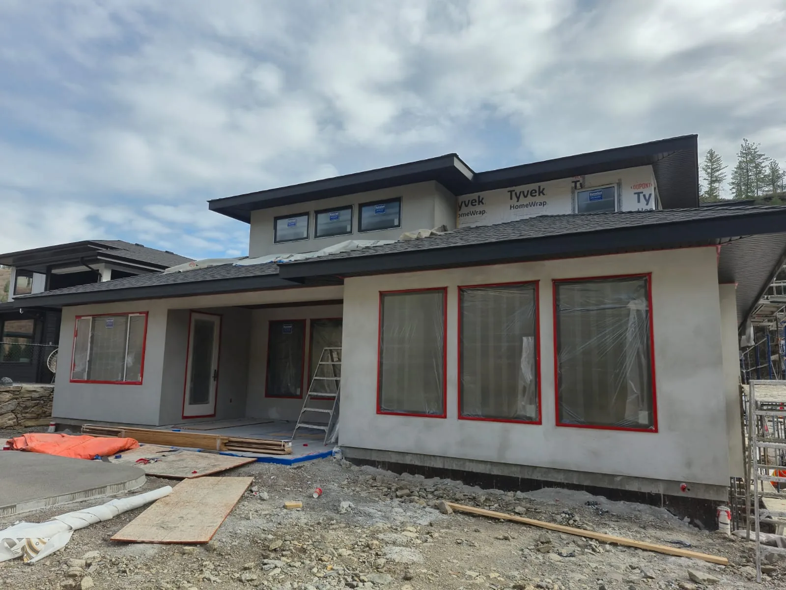 Patio corner of the Lot 42 home mid-project, grey stucco with windows masked in red tape.