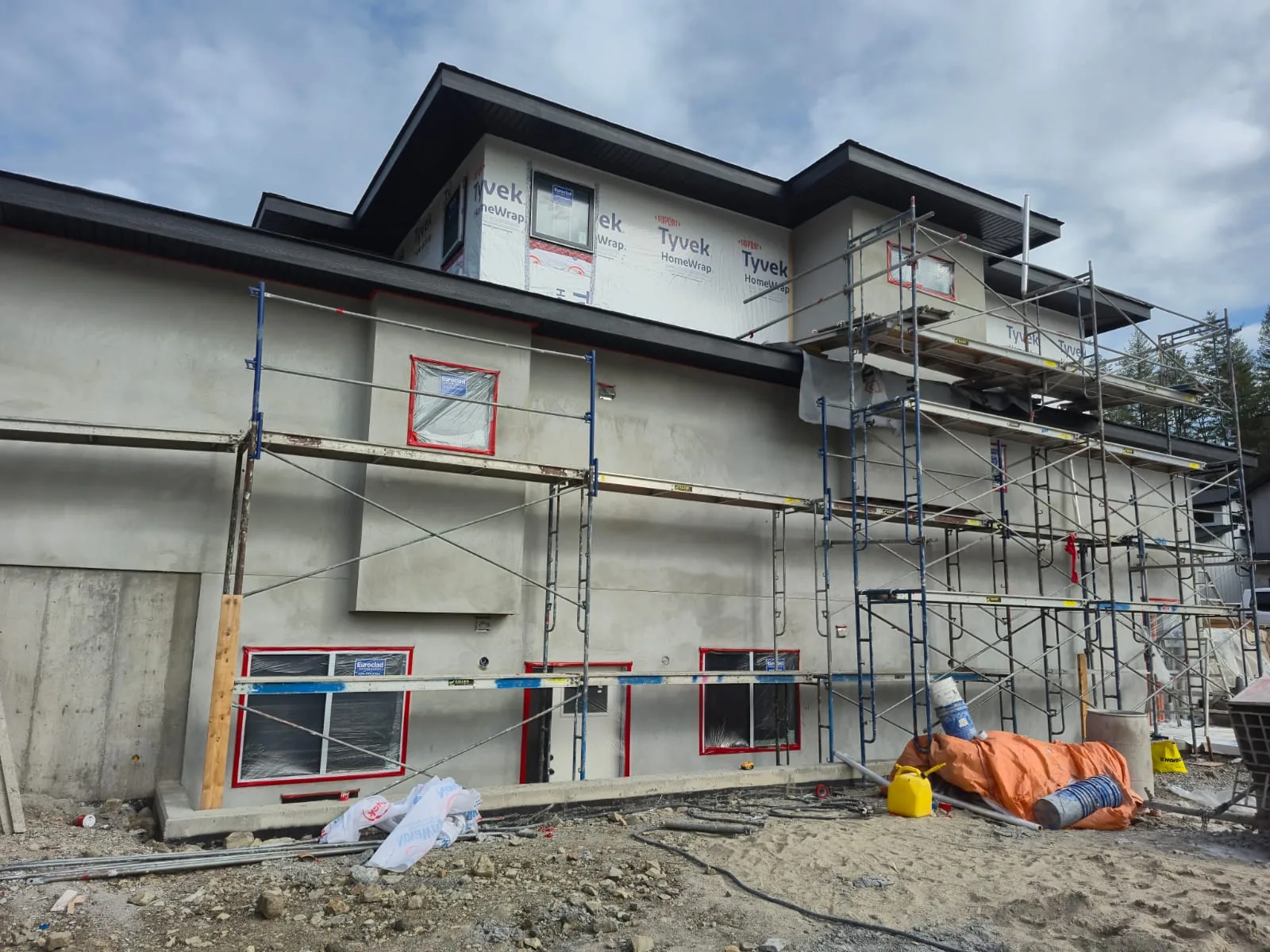 Scaffolding along a tall stucco side wall at Lot 42 during application, upper storey still in house wrap.